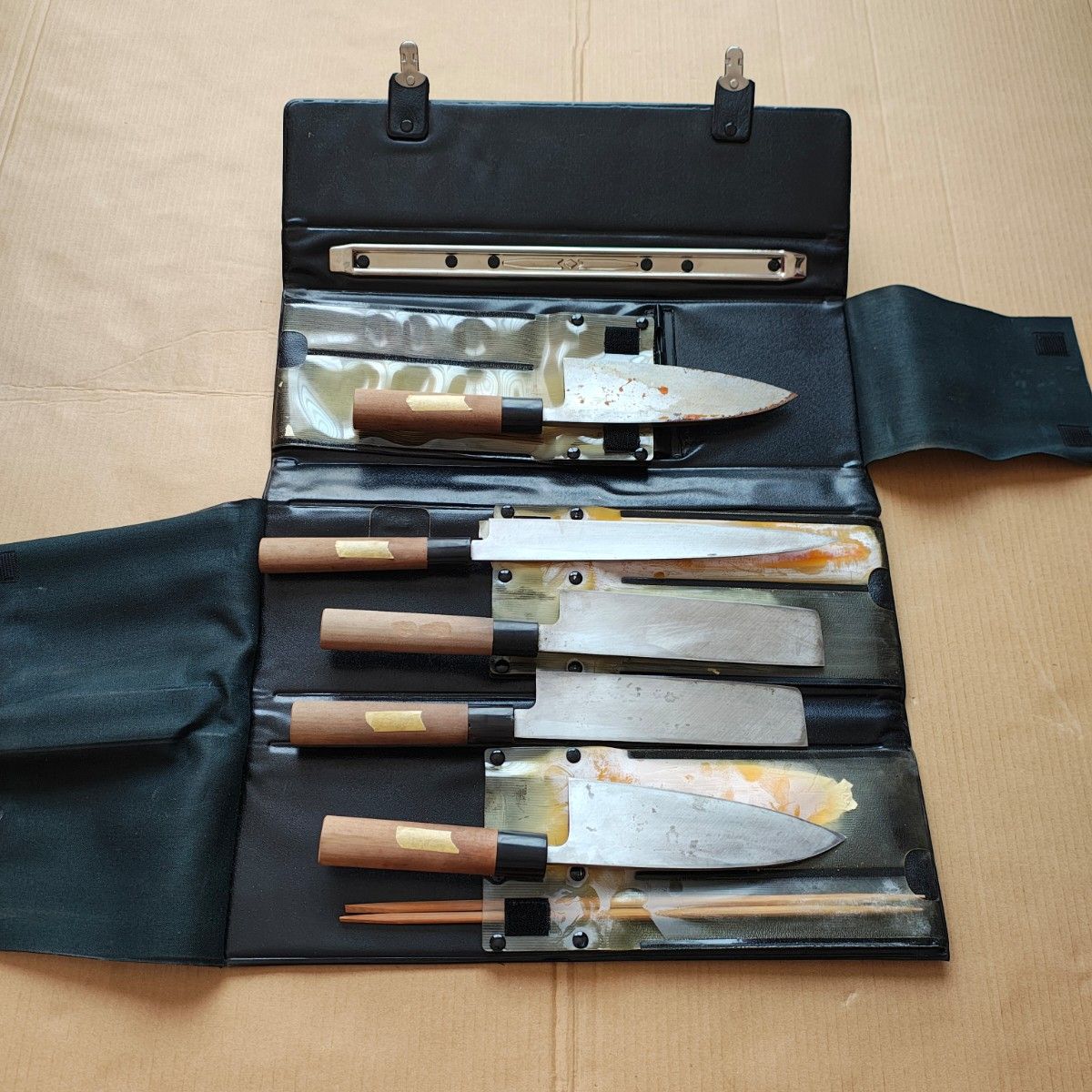 Five Japanese-style chef knives with wooden handles arranged in an open black roll-up case.