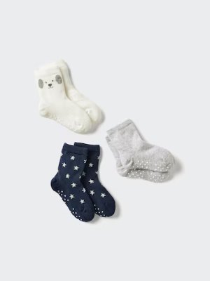 Three children's cotton socks laid flat: a white pair with an animal face, a navy pair with star pattern, and a gray pair with dotted grips.