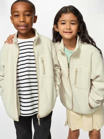 Two children wearing cream-colored fleece full-zip childrens jackets standing together against a white background.