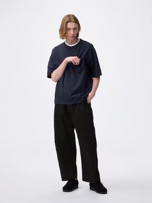 Male model wearing black chino barrel-leg pants and a dark T-shirt on a white background.