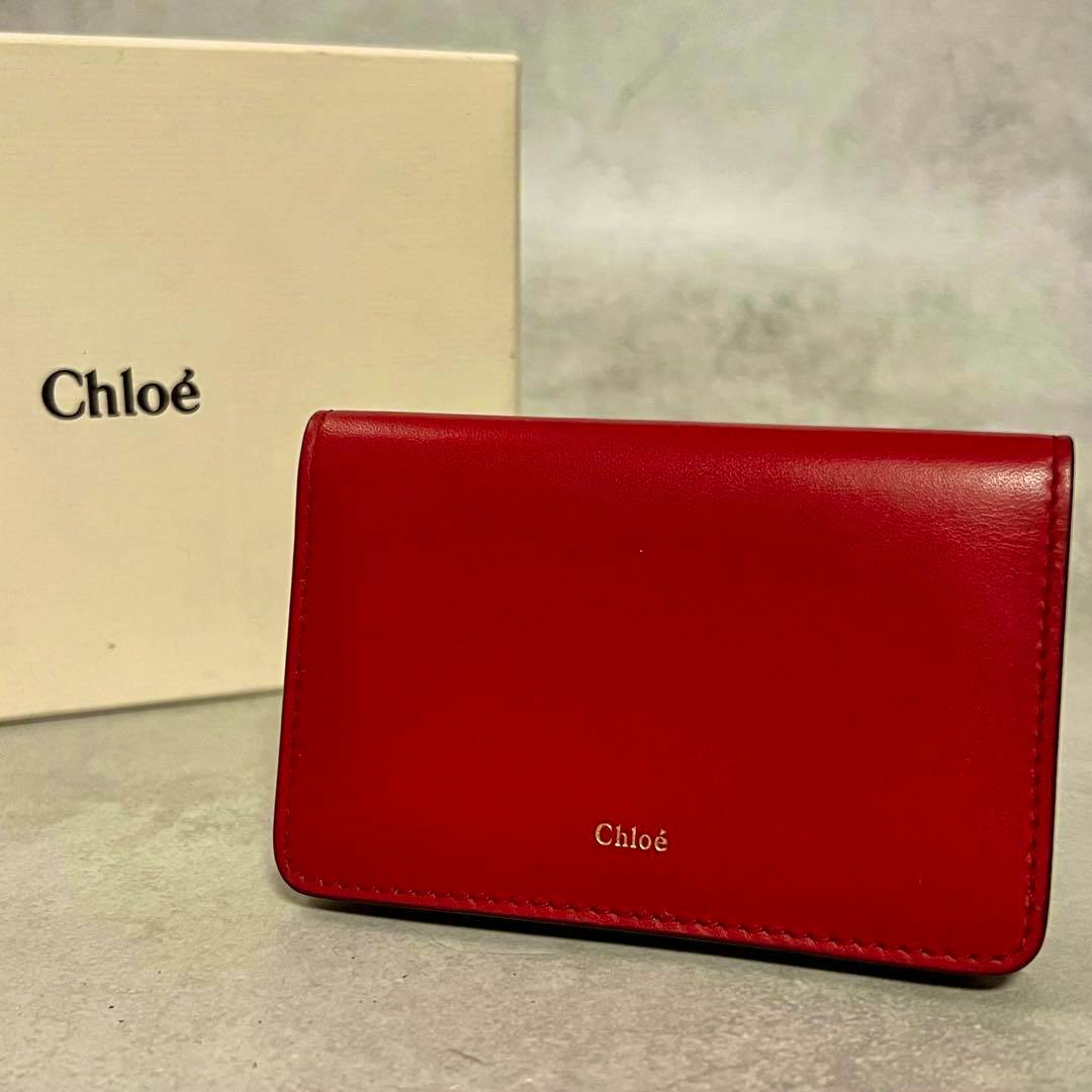 Red Chloé bicolor leather card case shown on a surface with a Chloé box in the background.