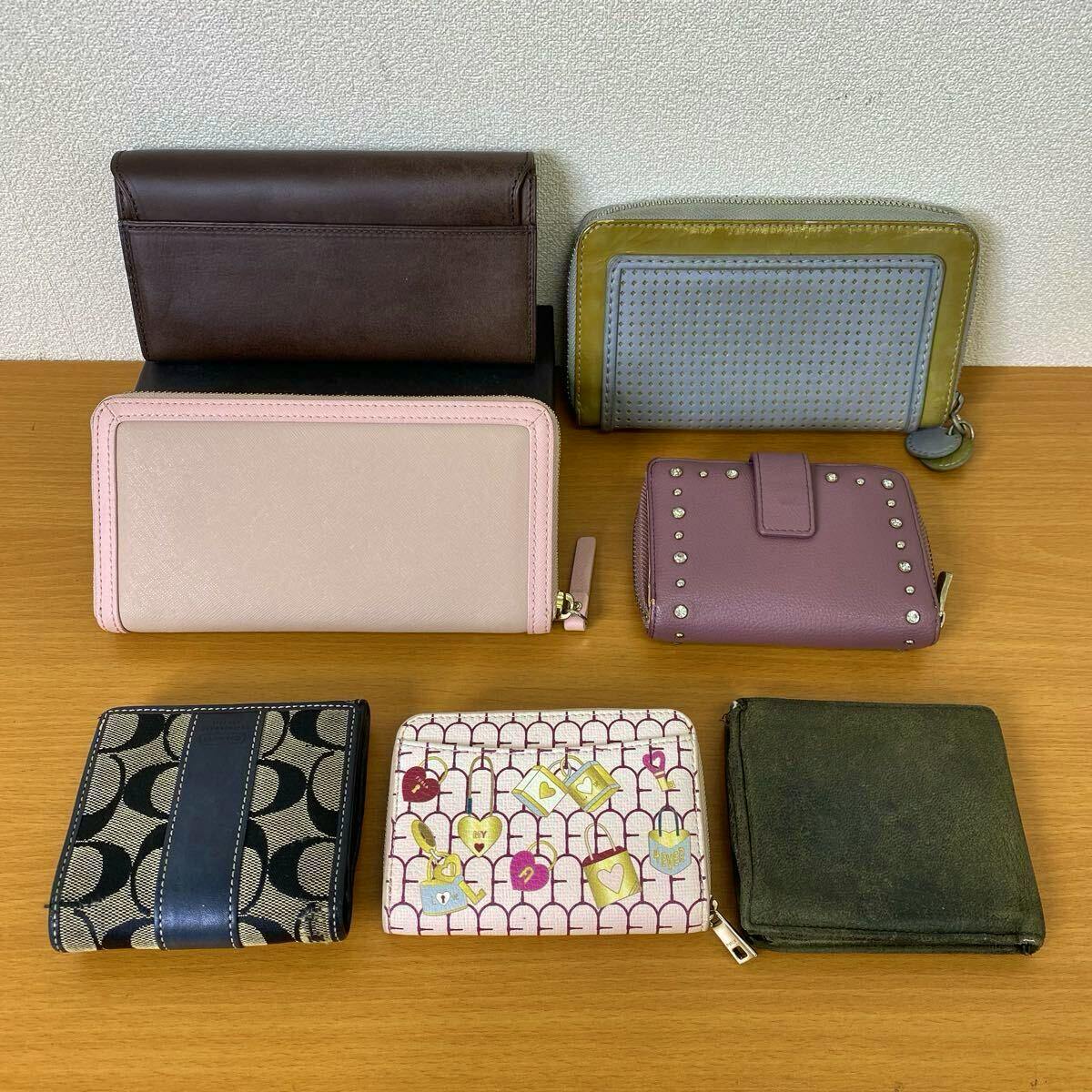 Seven assorted wallets and small purses arranged on a wooden surface against a wall.