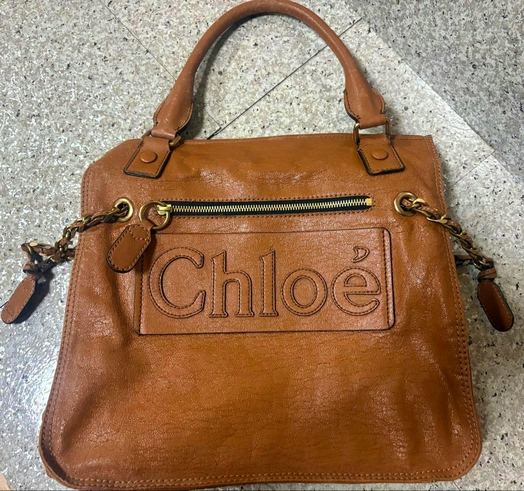 Brown leather Chloé handbag lying flat showing the embossed "Chloé" logo, front zipper pocket, and short handles.