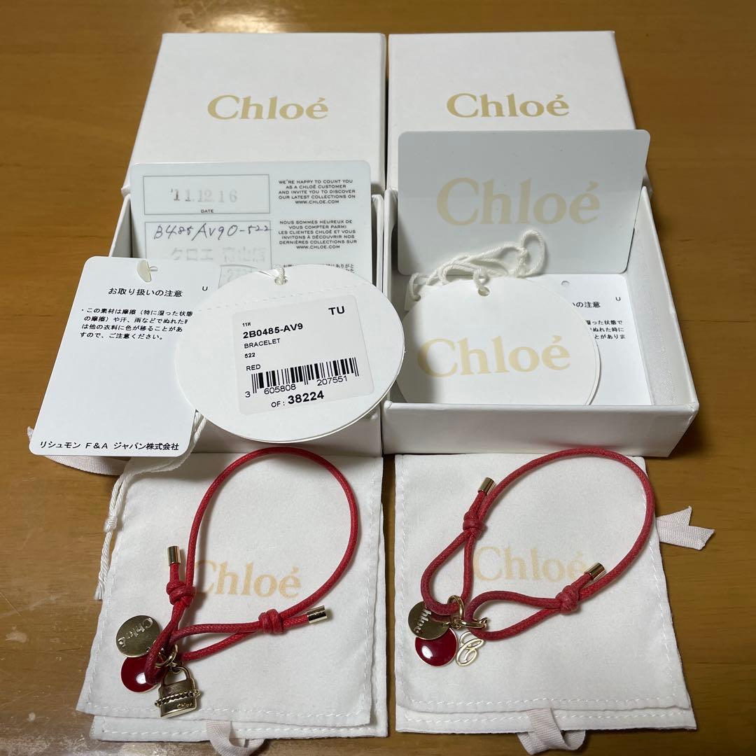 Two red leather cord bracelets with gold-tone charms displayed on Chloé branded pouches with Chloé boxes and tags in the background.