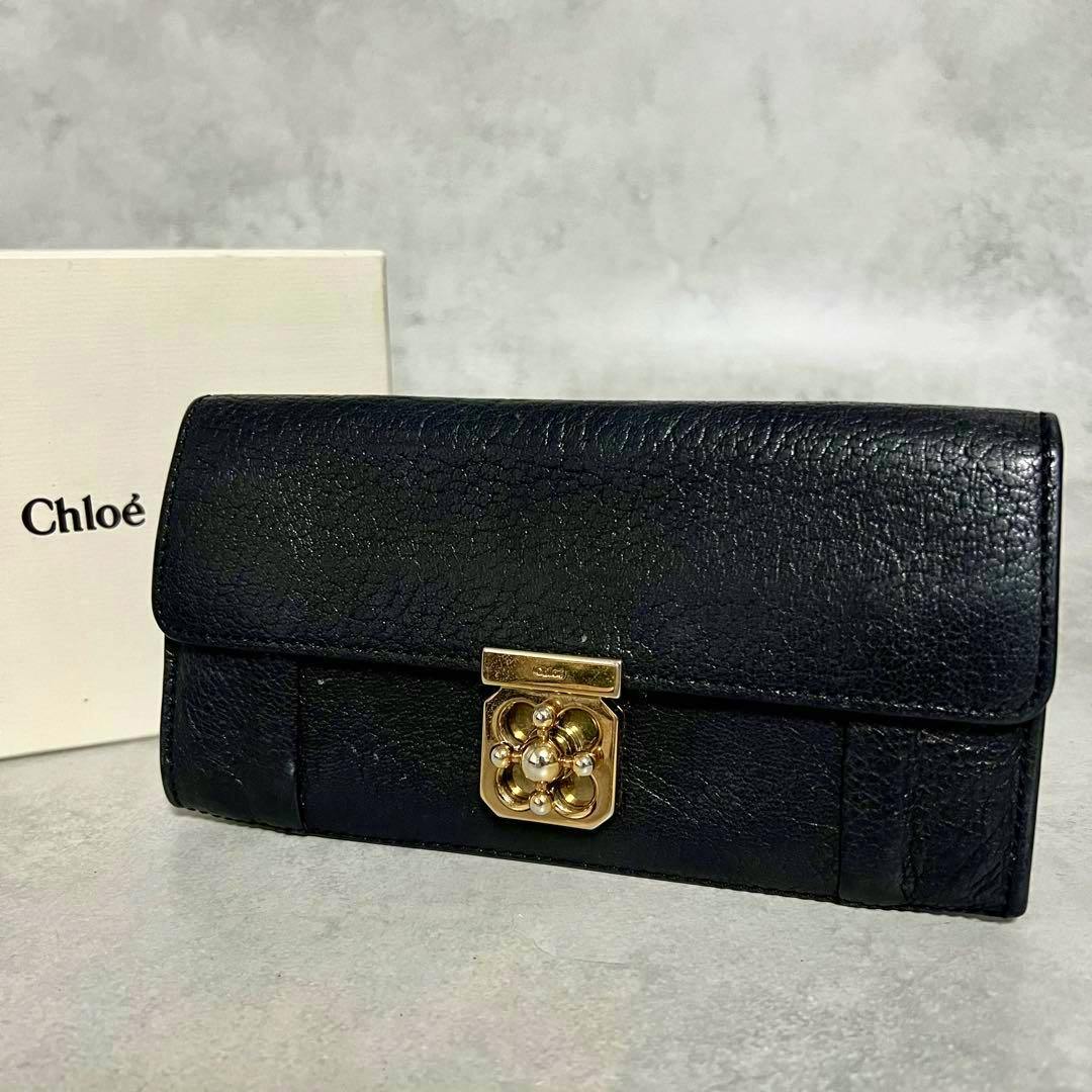 Front view of the black Chloé leather long wallet showing a gold turn-lock clasp with a Chloé box in the background.
