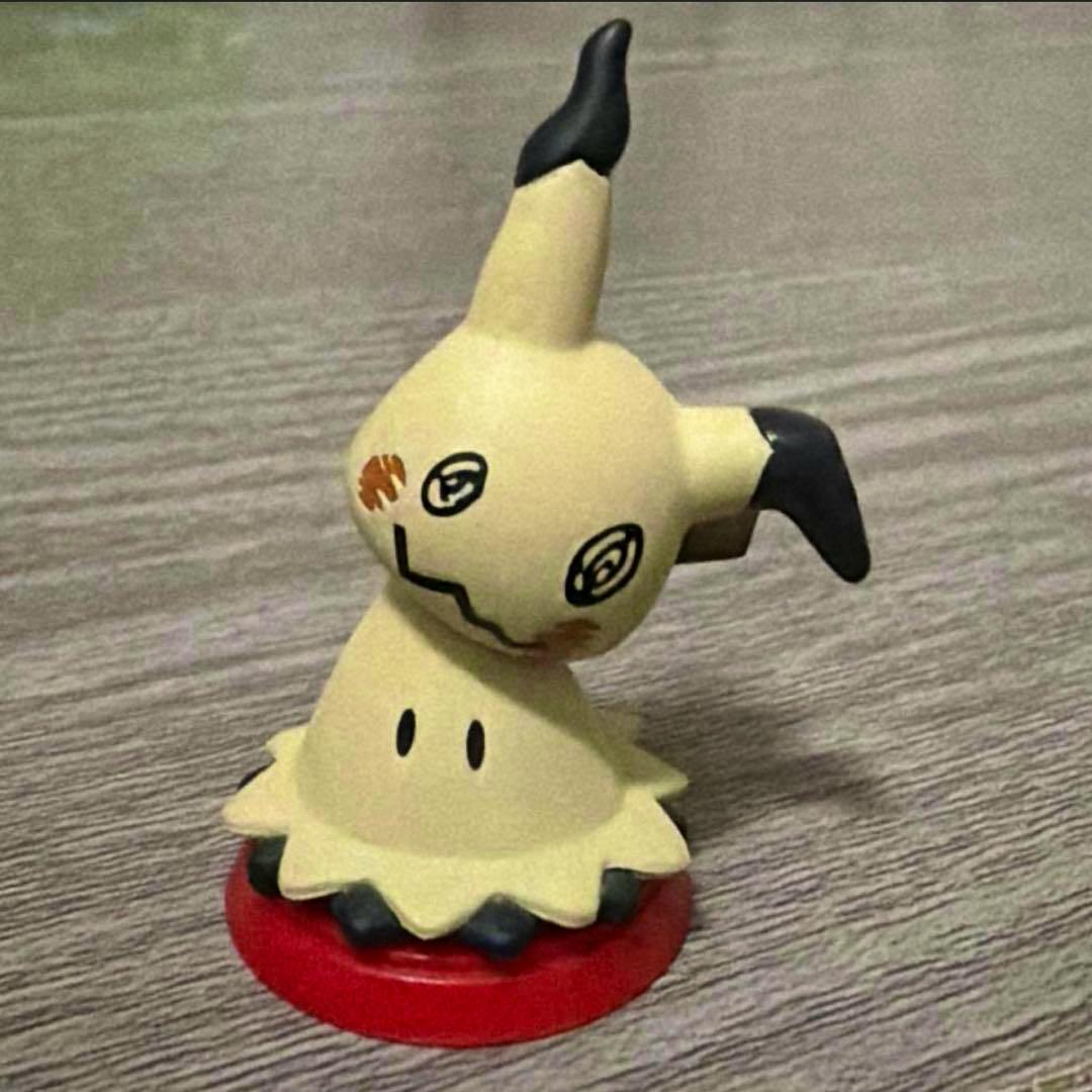 Front view of a small Mimikyu plastic figure standing on a red circular base.