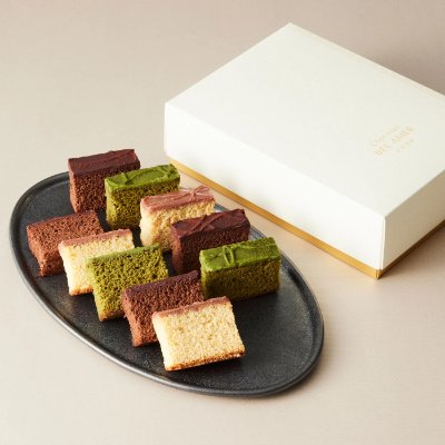 Ten small rectangular cake pieces arranged on a black plate next to a white gift box.
