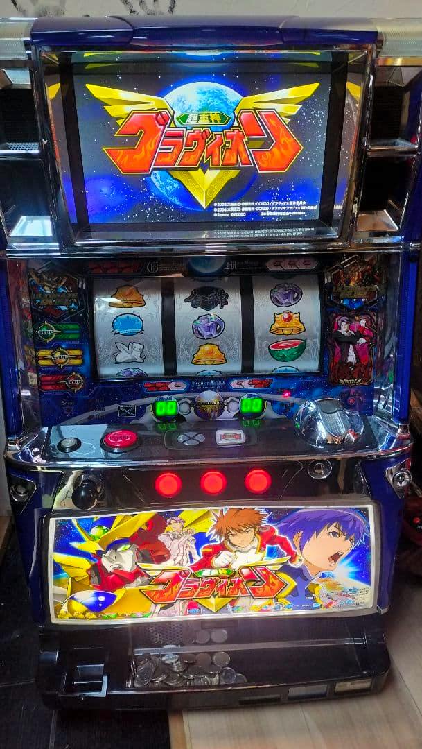 Front photo of the pachislot machine 超重神グラヴィオン showing the top display, three reels, control buttons, and illuminated lower artwork.