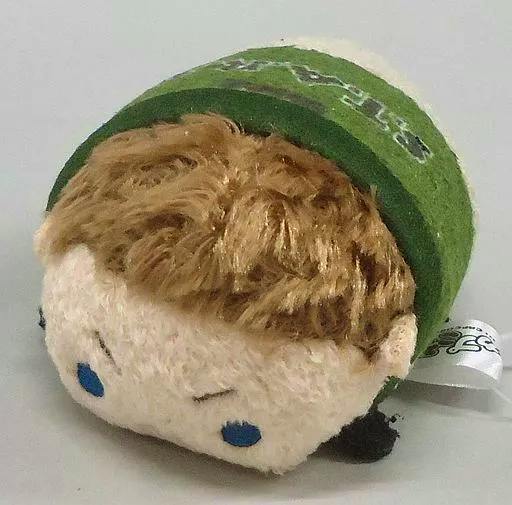 Plush keychain mascot of Chris Redfield in a green outfit lying on its side, showing brown hair, blue eyes, and a fabric tag.