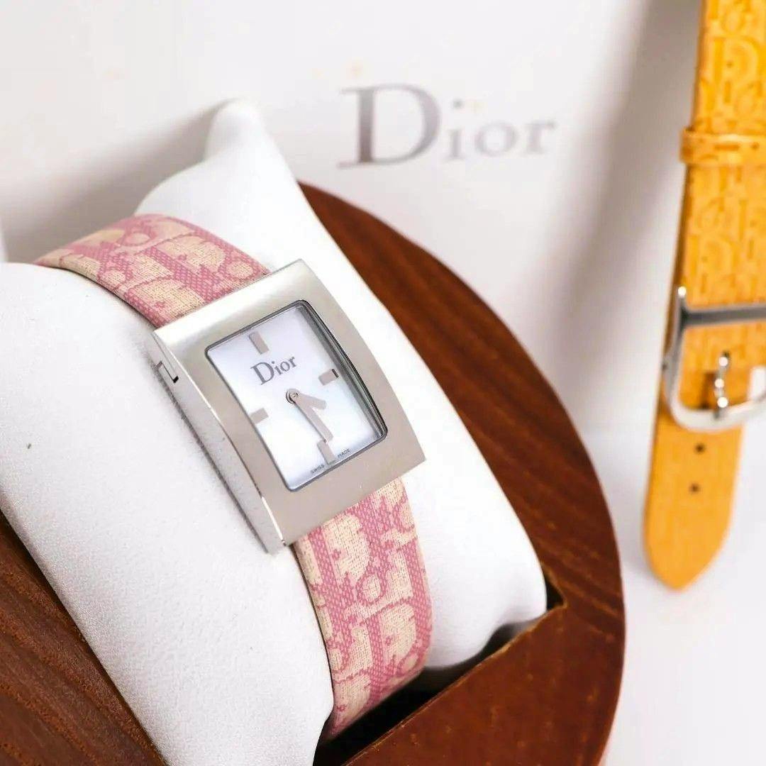 Rectangular metal-cased Christian Dior wristwatch with a pink patterned strap on a display pillow, with an additional yellow strap visible.