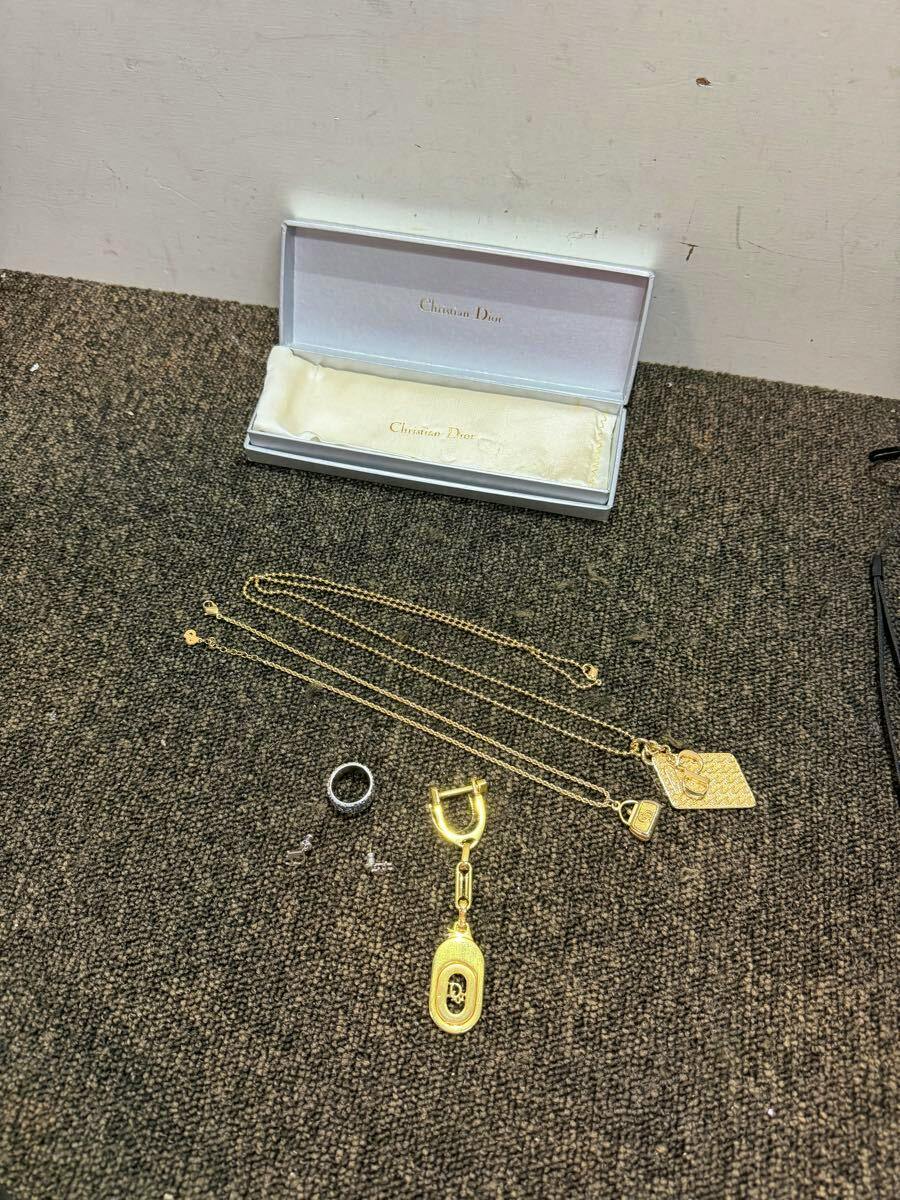 Christian Dior accessories set with two gold-tone necklaces, a gold key charm, a ring, small earrings, and an open Christian Dior case displayed on carpet.