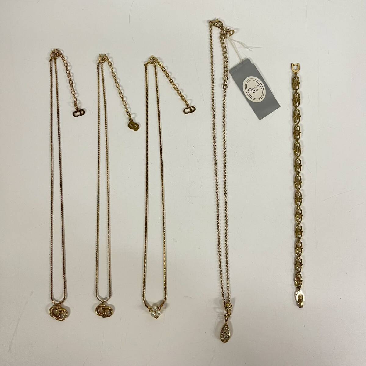 Five gold-color Christian Dior accessories (necklaces and a bracelet) laid flat on a white background.