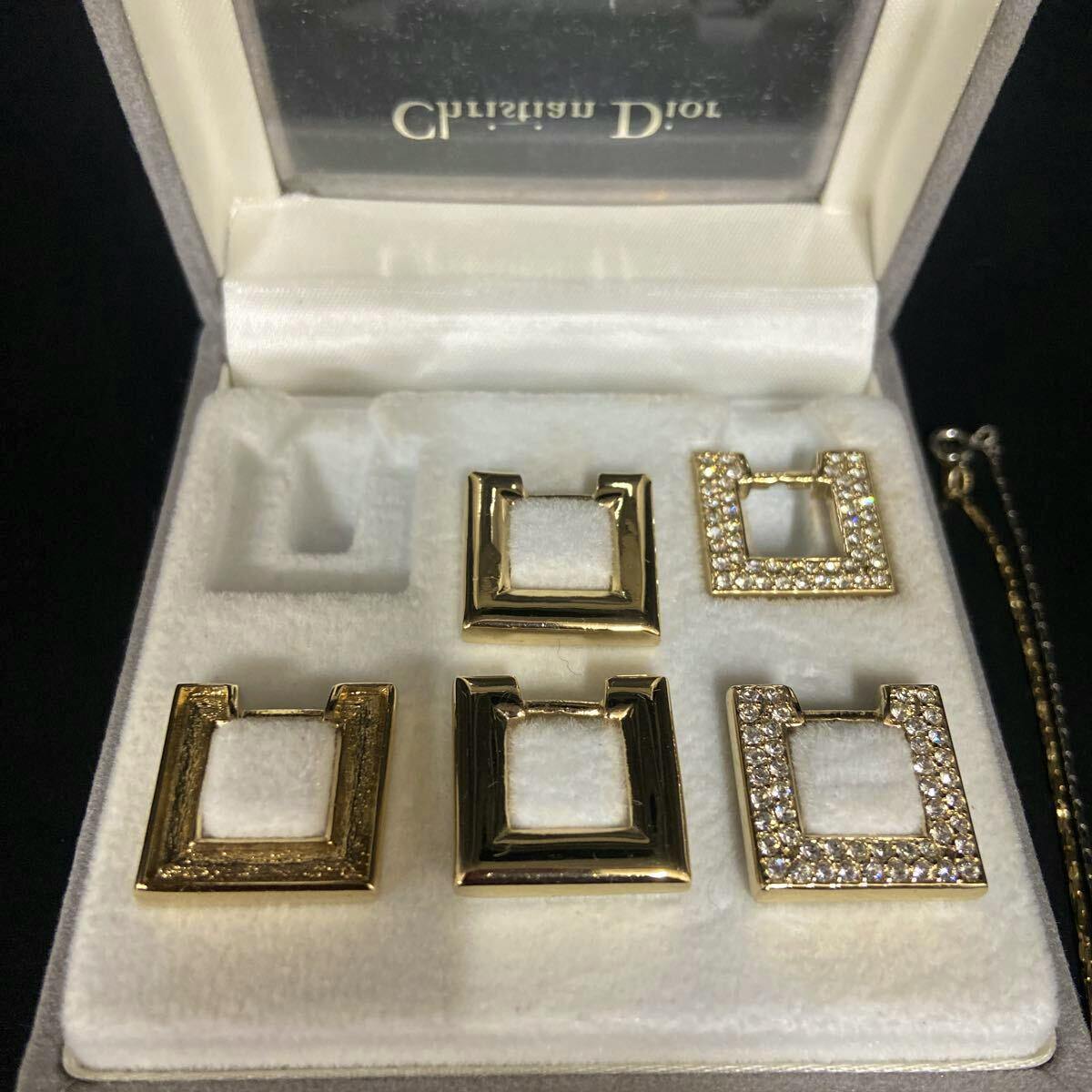 Close-up of a Christian Dior set of six square charm pieces displayed in a padded jewelry box with a chain visible at the right.