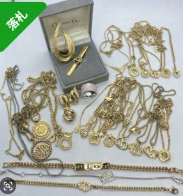 A laid-out assortment of gold-tone Christian Dior necklaces, bracelets, earrings and rings on a white background with a small Dior jewelry box.