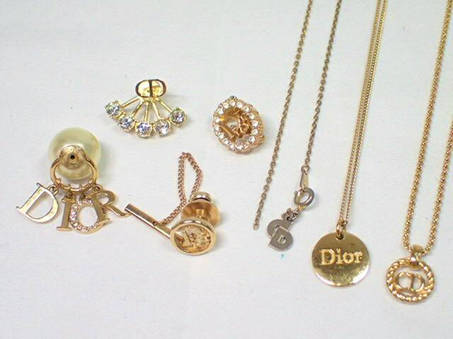 Close-up of several gold-tone Christian Dior accessory parts, including necklace pendants, earring components, and a tie pin on a white background.