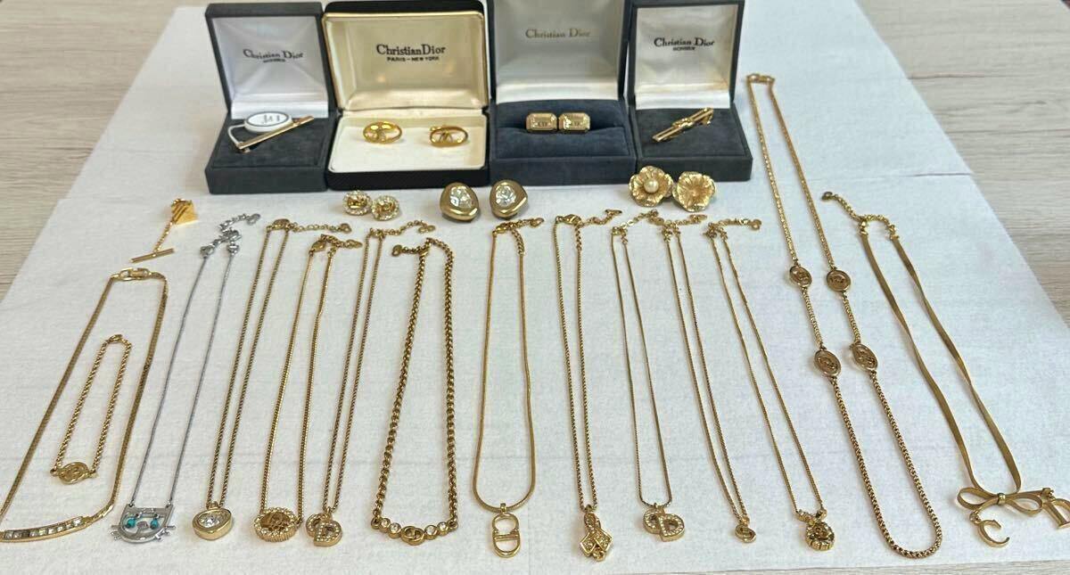 Multiple gold-tone Dior necklaces and other Dior accessories arranged flat on a light cloth with several Christian Dior jewelry boxes at the top.