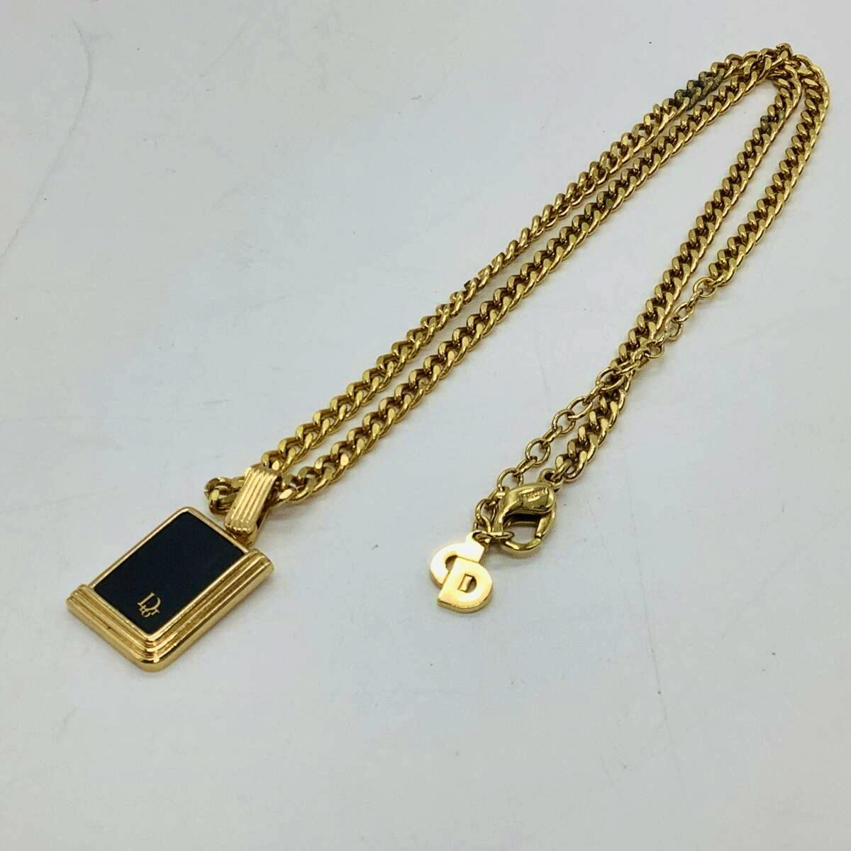 Gold-colored Christian Dior necklace with a black square pendant and a small CD charm laid flat on a white background.