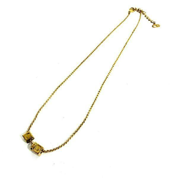 Christian Dior gold-colored necklace with cube-shaped CD charms on a thin chain laid flat on a white background.