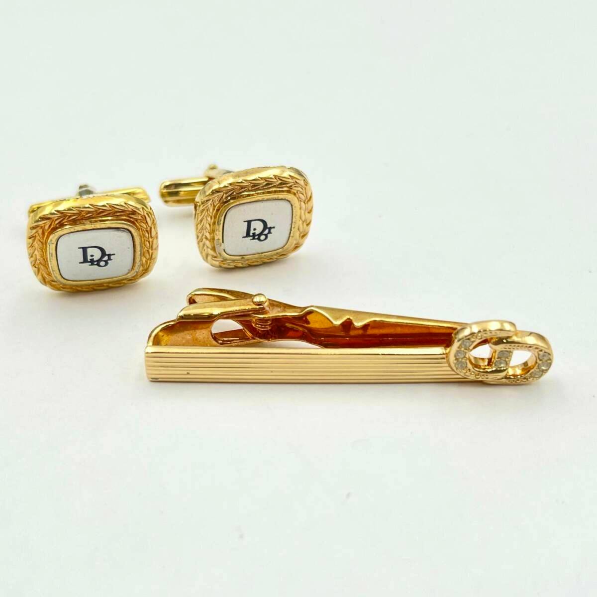 A pair of gold-tone Christian Dior cufflinks with white centers and a gold tie clip featuring a CD logo on a white background.