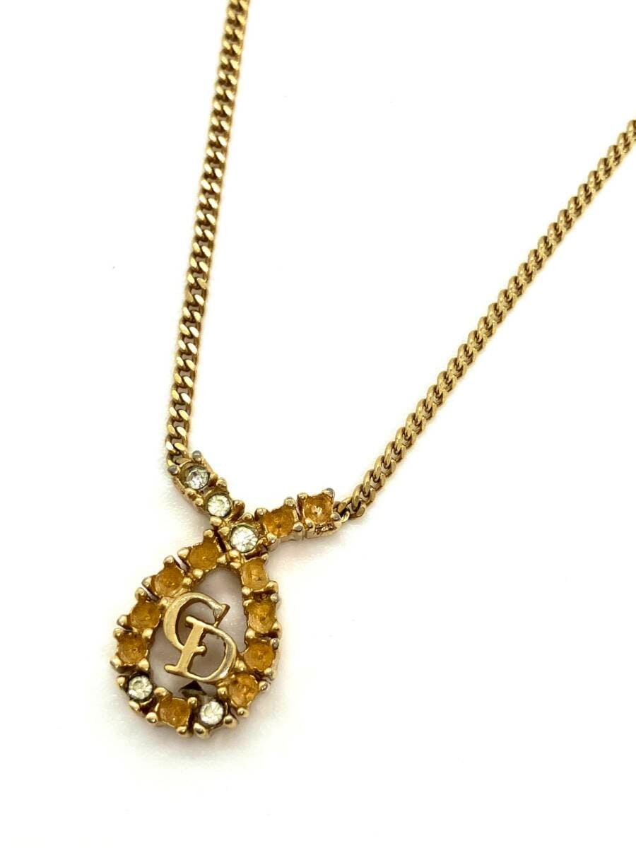 Gold Christian Dior necklace with a CD logo teardrop pendant surrounded by yellow and clear stones on a chain.