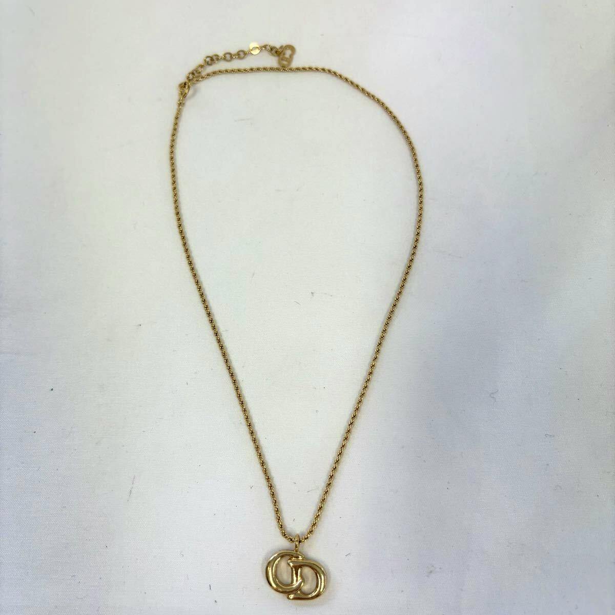 Gold-colored necklace with an interlocking CD logo pendant on a chain laid flat on a white background.
