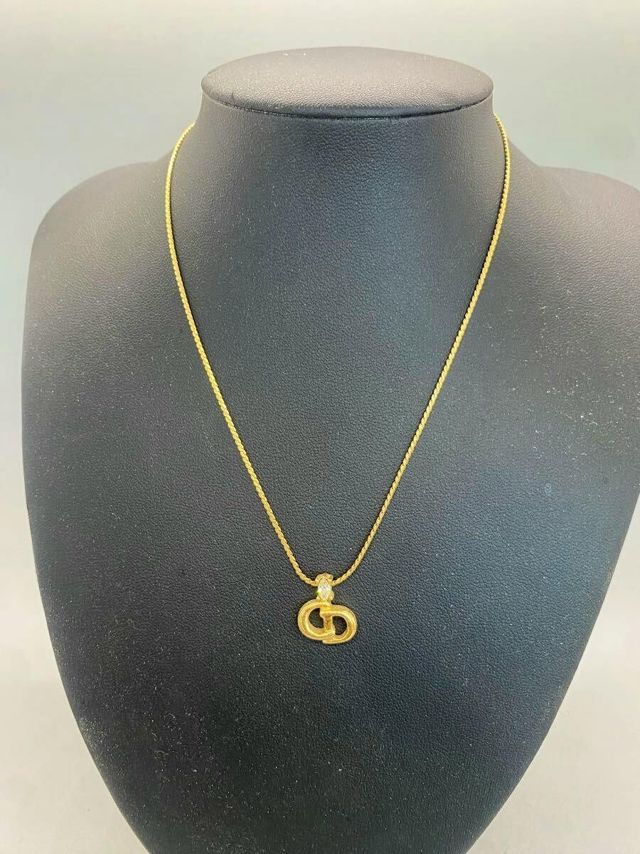 Gold-colored necklace with a CD logo pendant displayed on a black jewelry bust.