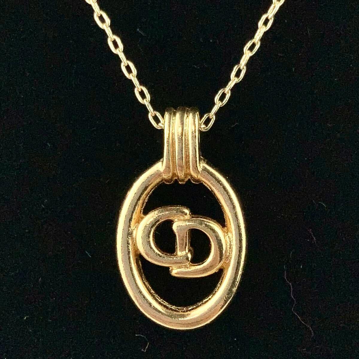 Close-up of a gold-colored CD logo pendant on a chain against a black background.