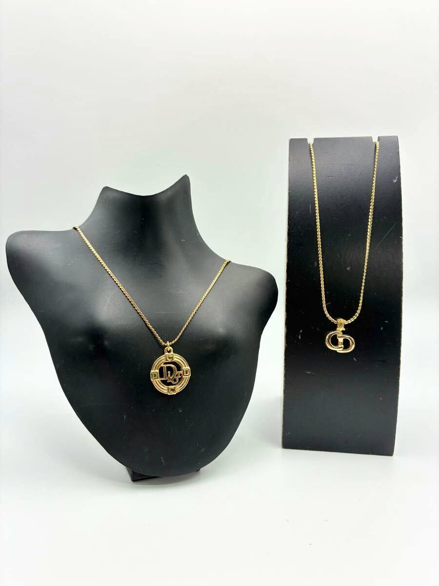 Two gold-color Christian Dior pendant necklaces displayed on black necklace stands.
