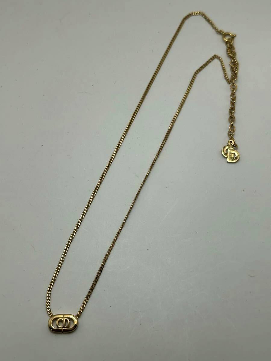 Gold-colored Christian Dior CD logo necklace laid flat on a white background showing the pendant, chain, and extension with a small CD charm.