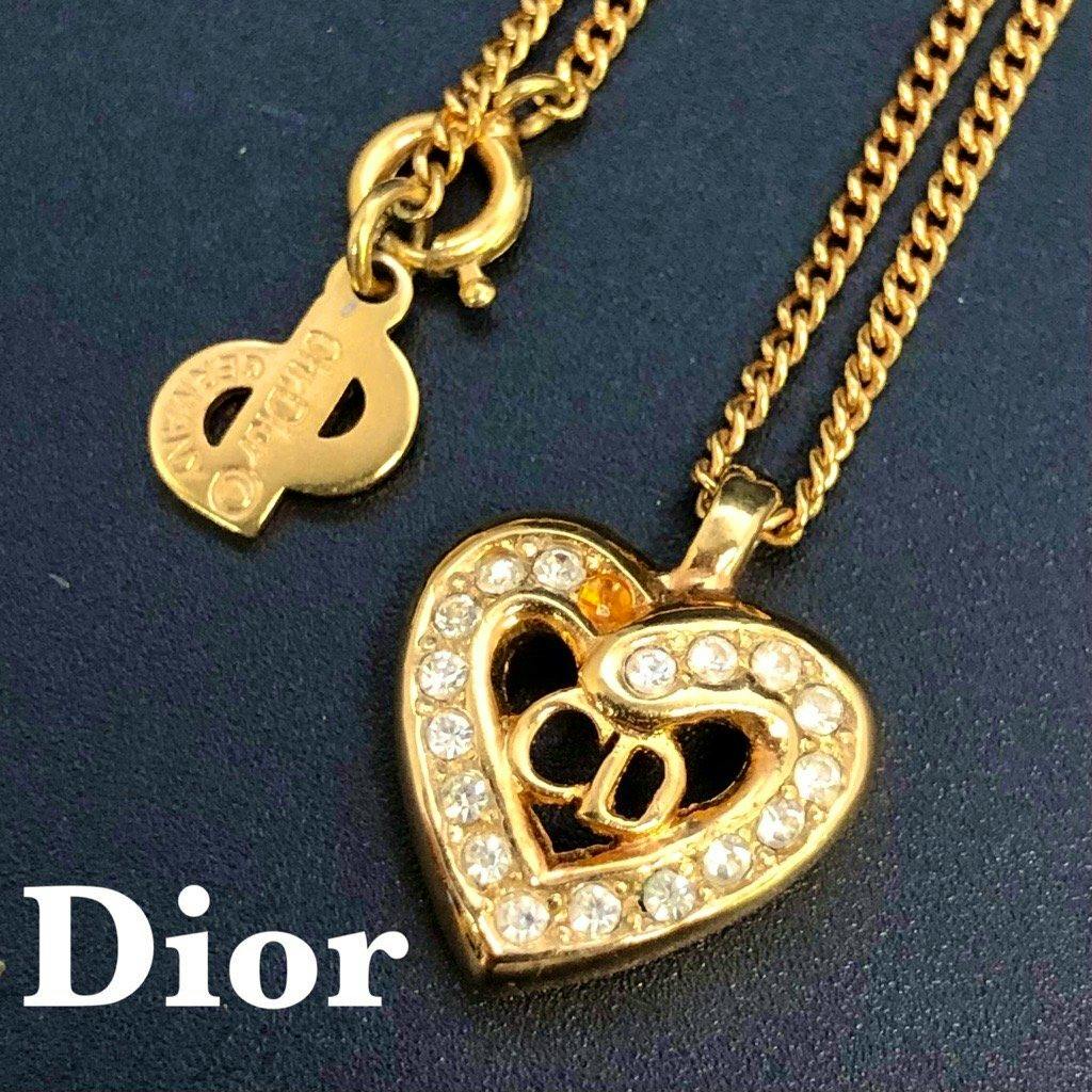 Gold-tone Christian Dior heart pendant necklace with rhinestones and a small Dior tag on a gold chain against a dark background.