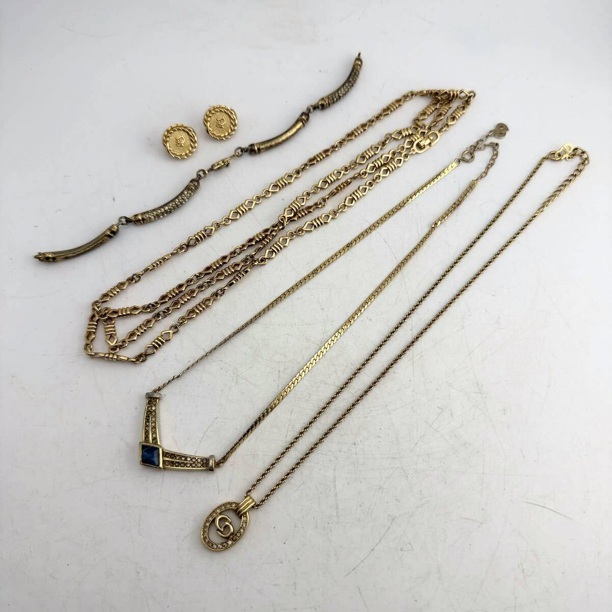 Several gold-tone Christian Dior necklaces and a pair of round Dior earrings arranged on a white background.