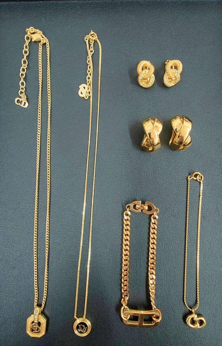 Gold-tone necklaces, bracelets, and earrings with CD logo charms arranged on a dark textured background.
