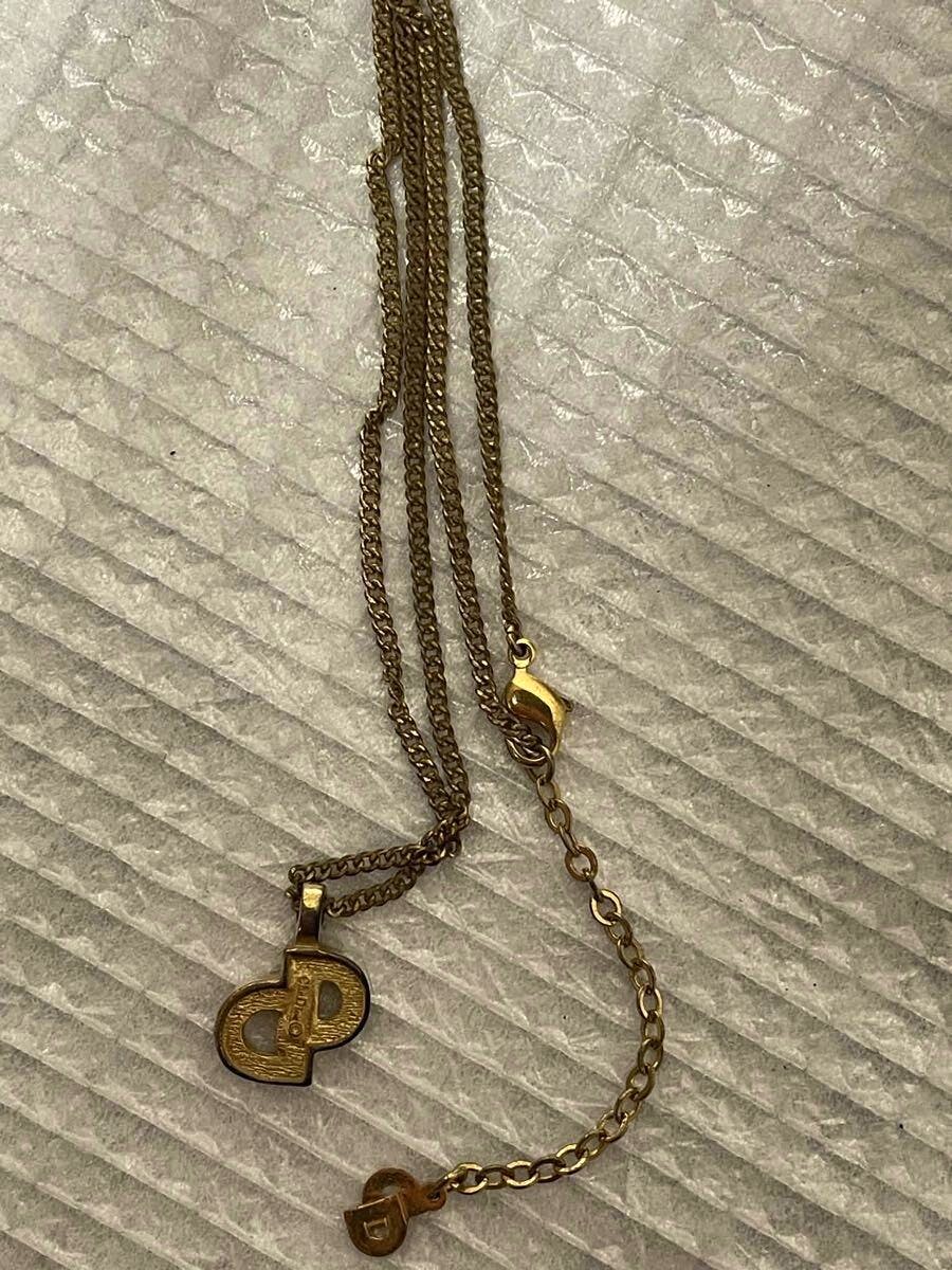 A metal necklace with a Christian Dior CD logo pendant, chain, clasp, and extender laid on a textured surface.