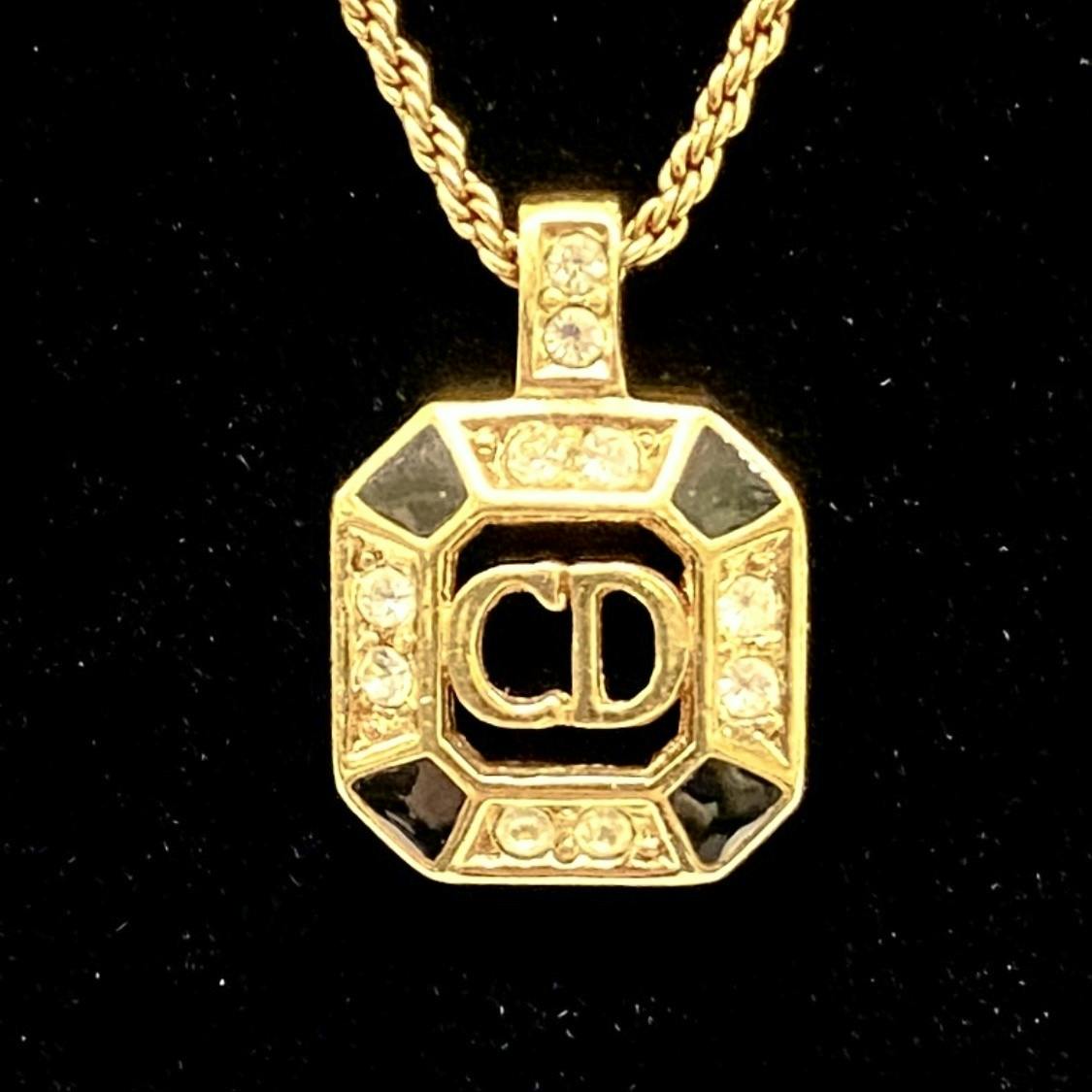 Close-up of a gold-tone Christian Dior octagon pendant with CD logo, black enamel accents and clear rhinestones on a gold chain.