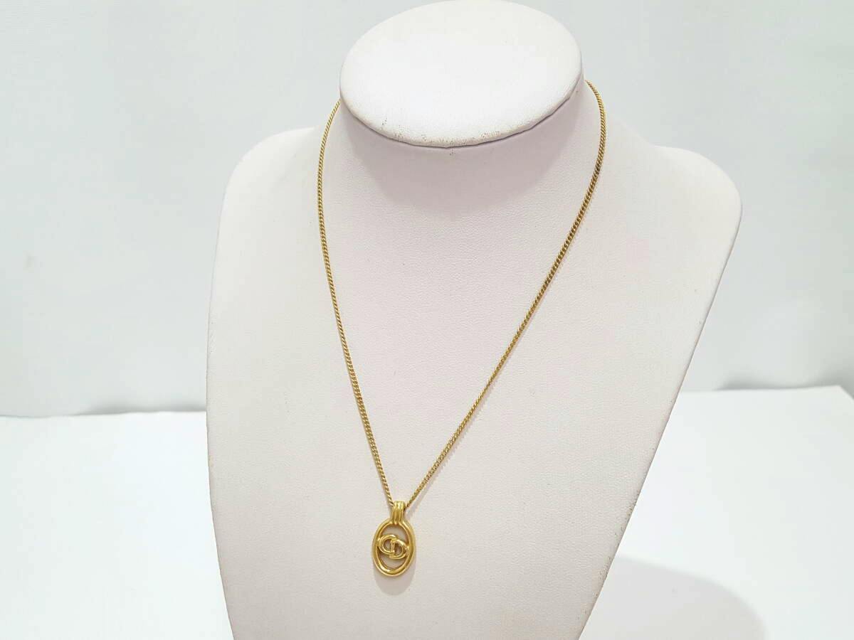 Gold-colored Christian Dior necklace with an oval CD logo pendant shown on a white display bust.