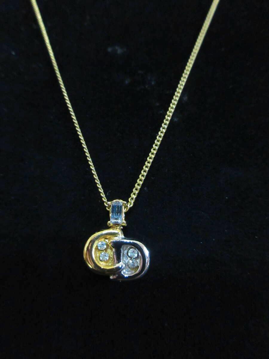 Gold and silver Christian Dior CD logo pendant necklace with rhinestones shown on a chain against a black background.