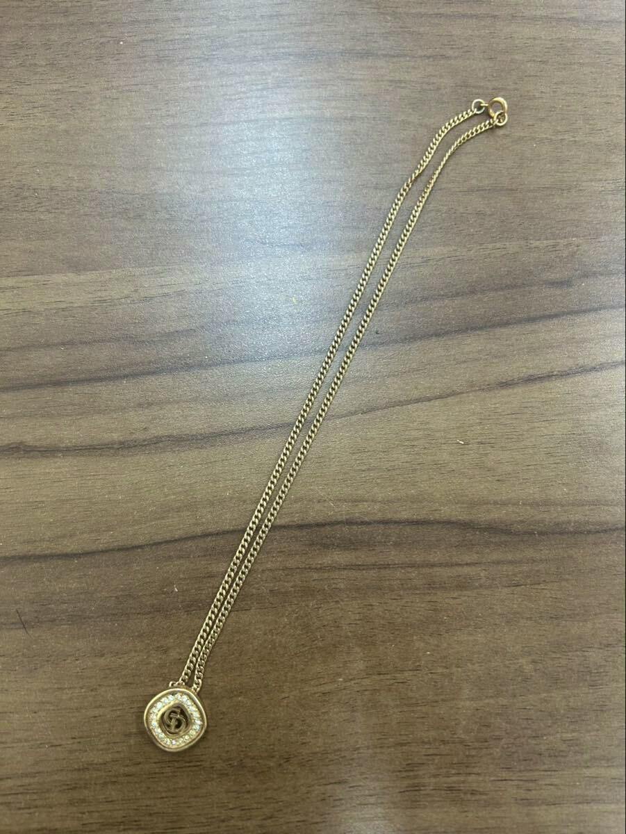 Gold-tone Dior necklace with a circular rhinestone-studded CD logo pendant laid on a wooden surface.