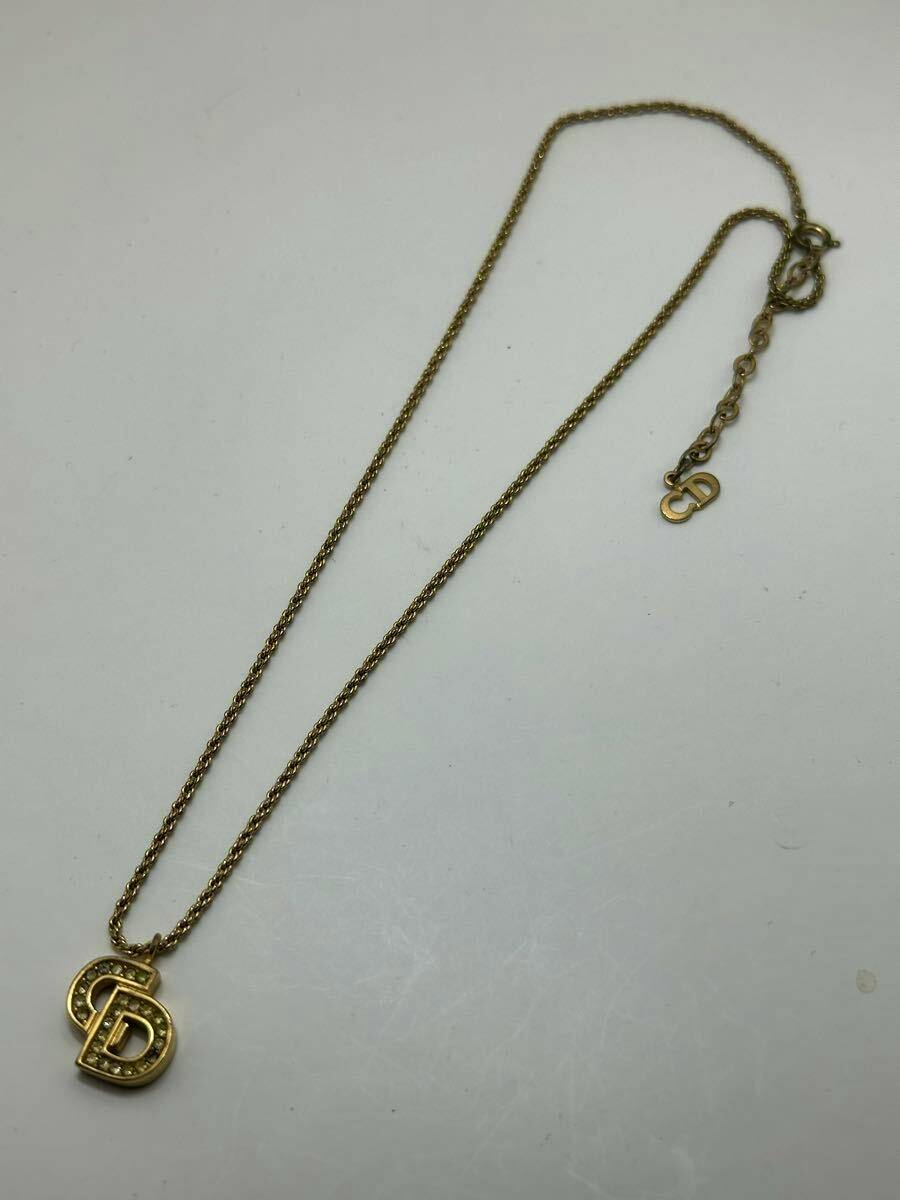 Gold-color Christian Dior CD logo necklace with a rhinestone-accented pendant on a white background.