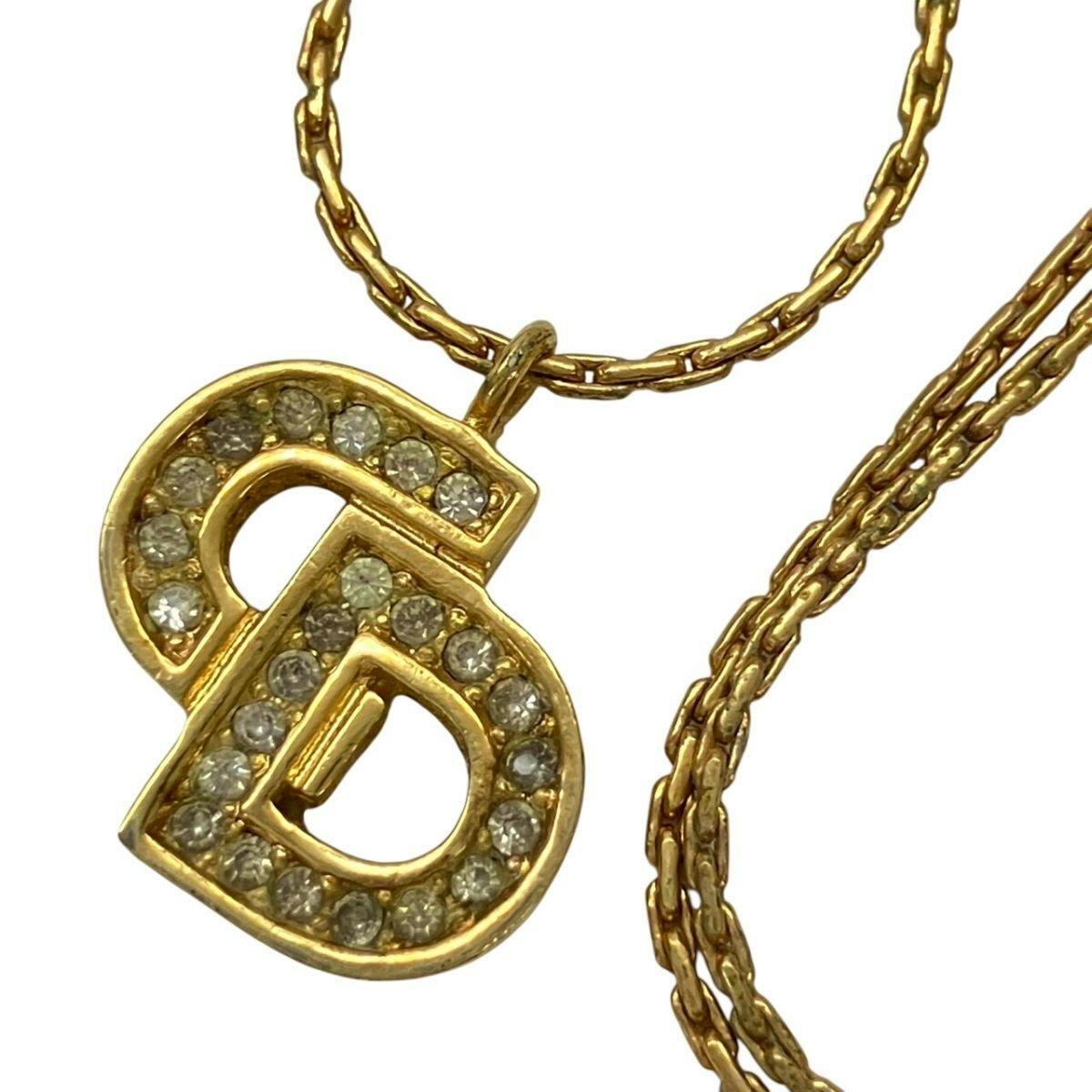 Close-up of a gold-color Christian Dior necklace showing the CD logo pendant with rhinestone accents on a gold chain.