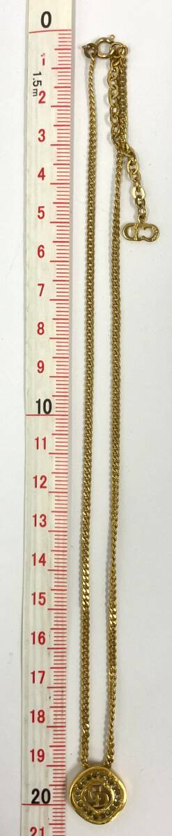 Gold-colored Christian Dior necklace with round CD-logo pendant and chain laid next to a measuring ruler.