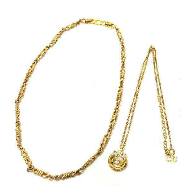 Two gold-tone Christian Dior necklaces on a white background; one has a circular CD logo pendant with rhinestone accents.