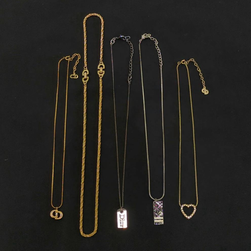 Five Christian Dior necklaces and pendants arranged on a black background, showing the five-piece accessory set.