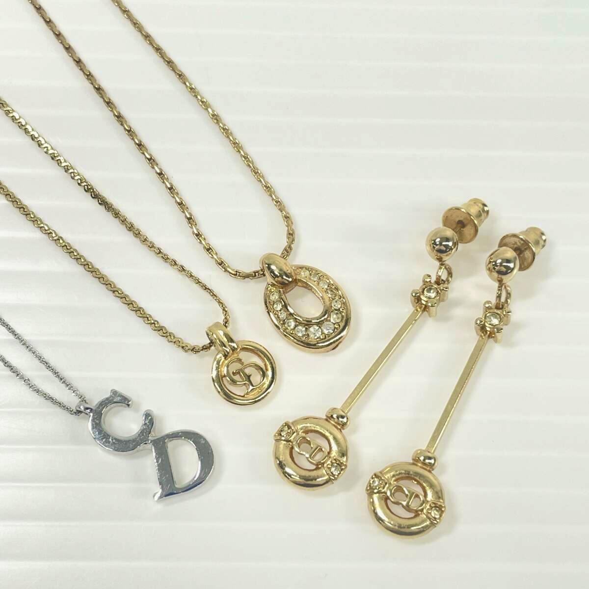 Gold and silver Christian Dior necklaces and a pair of long gold Dior earrings laid on a white textured background.