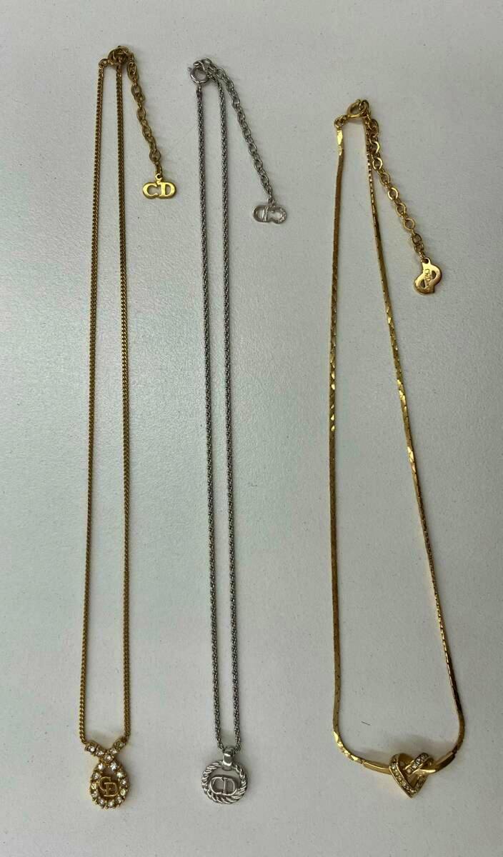 Three Christian Dior necklaces laid flat on a white surface, showing their chains and pendants.