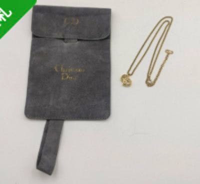 Gold-tone Christian Dior CD logo necklace laid next to a gray Christian Dior pouch.