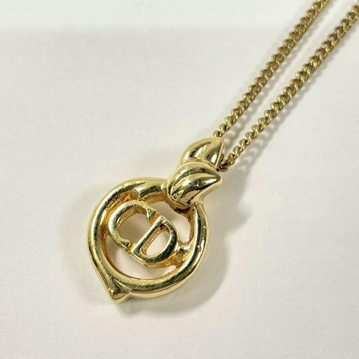 Gold-colored Christian Dior CD logo pendant necklace with chain laid flat on a white background.