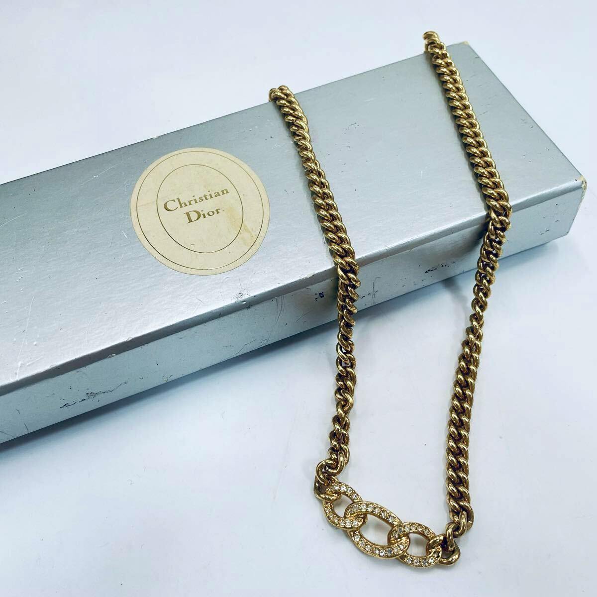 A gold-colored Christian Dior necklace with a three-link rhinestone centerpiece laid across a silver Christian Dior box.