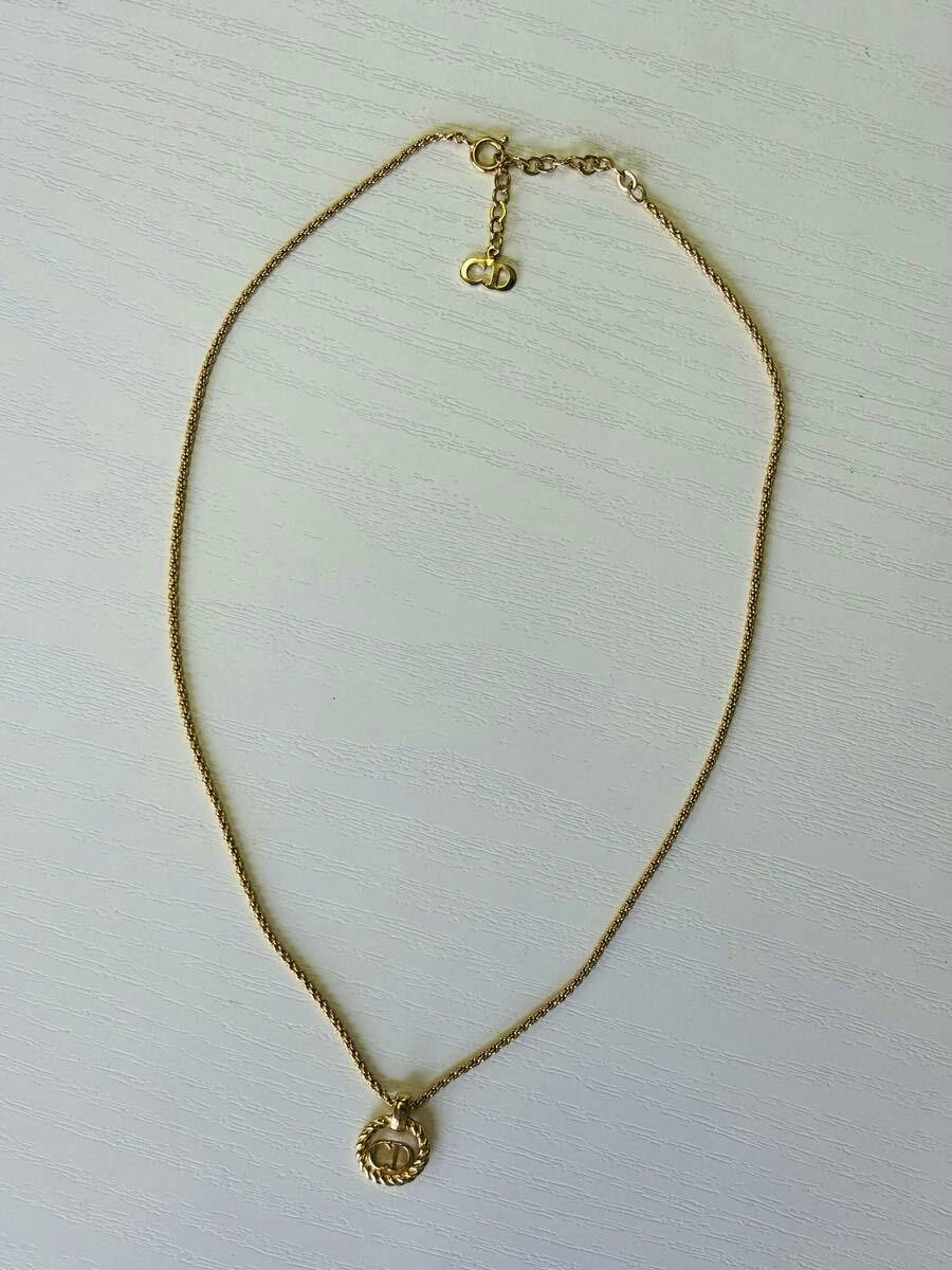 Gold-tone necklace laid flat on a white surface with a twisted circle pendant bearing a CD logo.