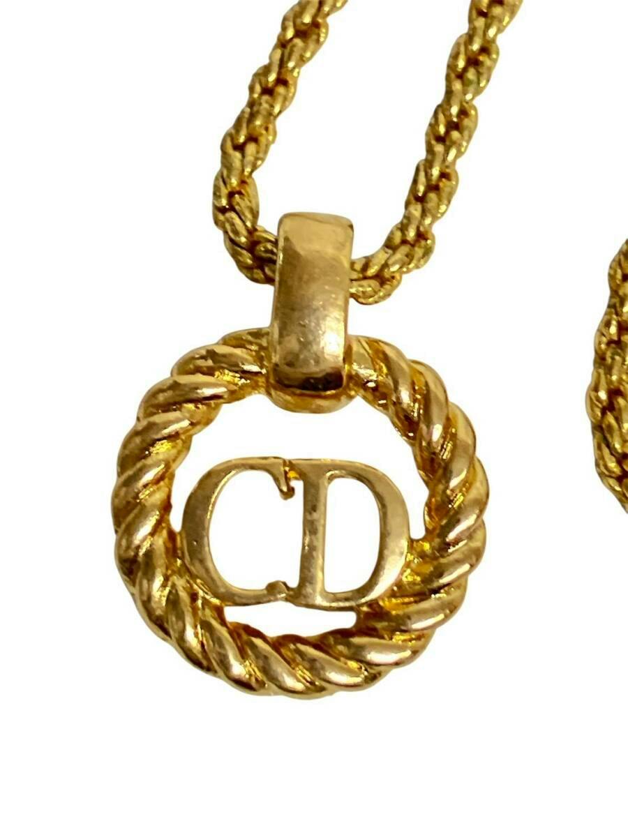 Close-up of a gold-color Christian Dior necklace pendant showing a twisted circle with CD logo and attached gold chain.