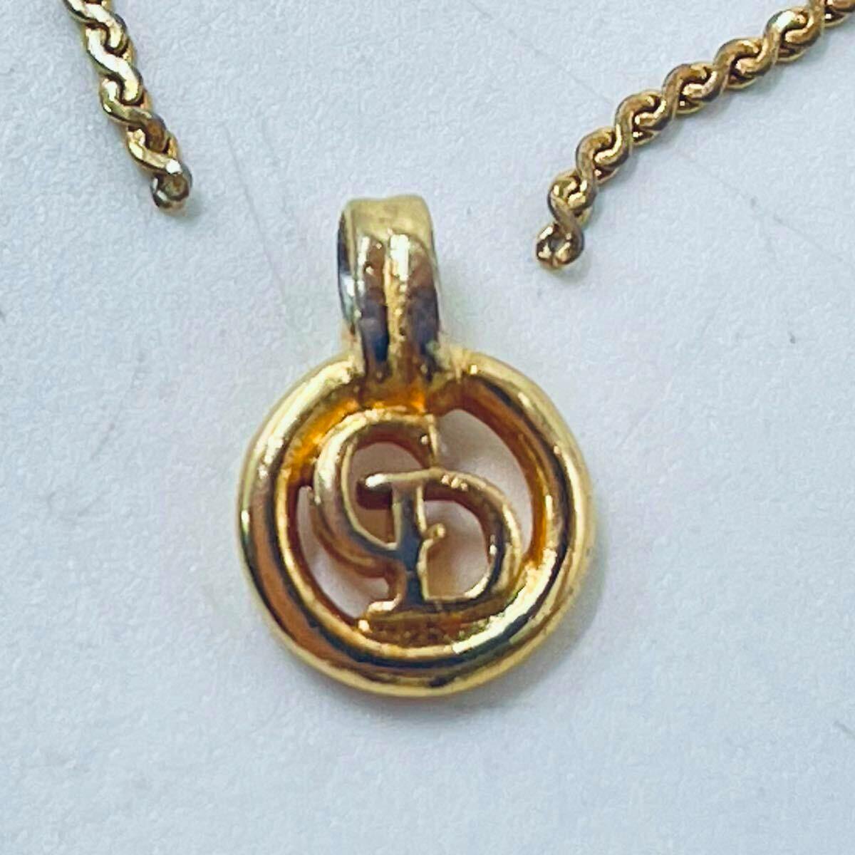 Close-up of a gold-tone circular Christian Dior pendant with interlocking CD logo and part of a gold chain.